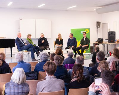 Menschen bei einer Diskussionsveranstaltung, Blick aus dem Publikum auf das Podium