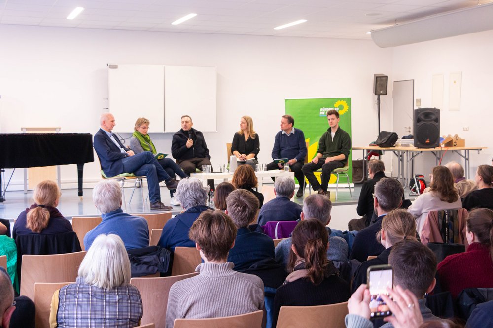 Menschen bei einer Diskussionsveranstaltung, Blick aus dem Publikum auf das Podium